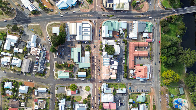 Top down Arial view of a small rural town centre with cars on the road, roof tops of homes and businesses, a river with park and trees. Main road with 4 Way intersection. Denmark Western Australia 