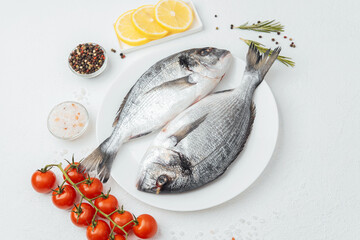 Close up of two dorado fish on white plate with lemon and tomato