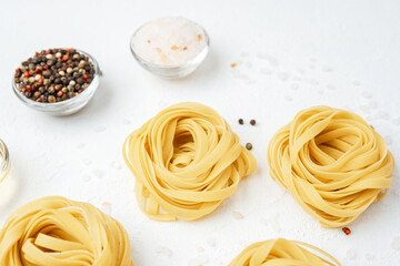 Raw tagliatelle pasta nests with tomatoes and spices on white background