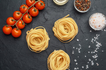 Closeup of tagliatelle pasta nests with tomatoes and spices on dark surface