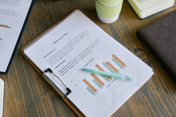 Closeup of marketing survey report with bar chart and pen resting on clipboard placed on wooden...