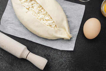 Raw khachapuri with cottage cheese and ingredients on black background