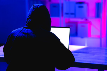Dark Figure in Hoodie Using Laptop in a Dimly Lit Environment