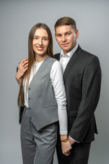 Young stylish couple. Guy and girl in classic clothes posing on white background in studio. Both are looking directly into camera. Modeling shoot, fashion and style concept.