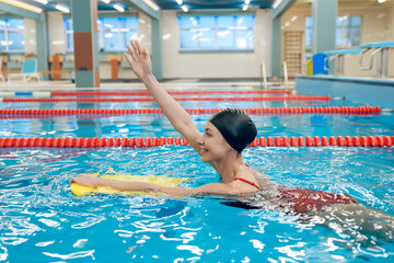 Cute caucasian young woman swimming in the pool with a board