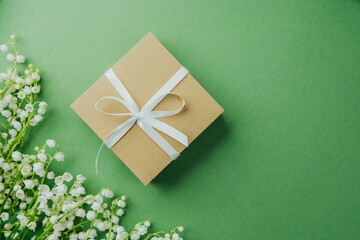 Gift box with white ribbon and lily of the valley flowers on green background