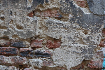 Red bricks visible beneath the peeling plaster of a wall