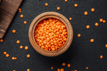 Bright orange lentils in a wooden bowl against a dark background