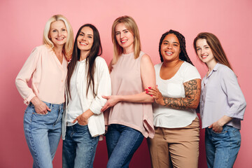 Five beautiful women of different ages and ethnicities are posing together on pink background