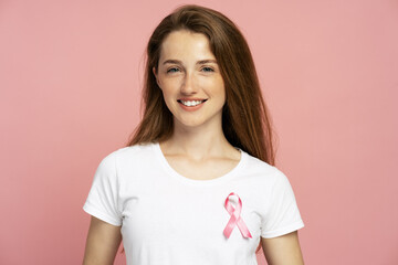 Young woman wearing pink ribbon supporting breast cancer awareness on pink background