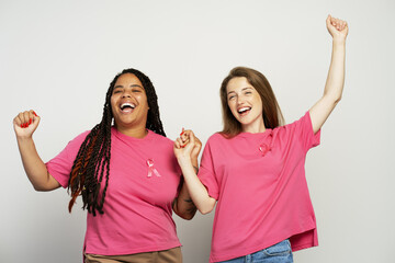 Two happy women celebrating breast cancer awareness holding hands and raising arms