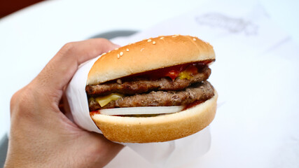 A double meat burger with ketchup and mustard on it, sitting in paper takeout container