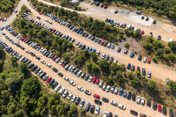 Top-down view of a large dirt parking area filled with neatly arranged cars in a Mediterranean...