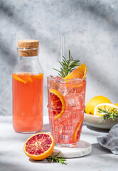 Blood orange cocktail with ice and rosemary on a marble stand on a gray background with shadows