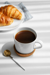 Coffee espresso cup and fresh croissants on a plate  on a white background with morning shadows.
