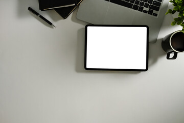 Top view of digital tablet with blank screen, laptop, notebook, and coffee cup on a white desk