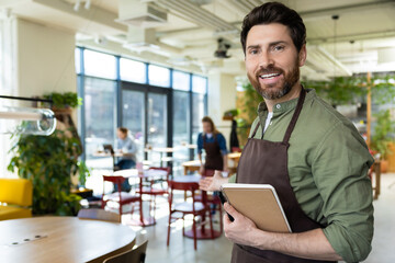 Young bearded man in apron looking confident while waiting for the client in pizzeria