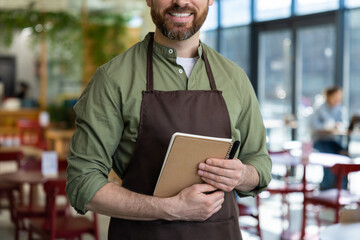 Young bearded man in apron looking confident while waiting for the client in pizzeria