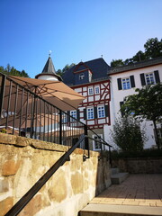 Sanierte alte Häuser in Naturfarben mit Fachewerk und Sonnenschirm vor blauem Himmel im...
