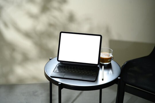 Digital tablet with blank screen on a black round table next to coffee cup and digital pen