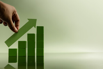 Hand placing green arrow on stacked bars, representing financial growth, rising profits, successful...