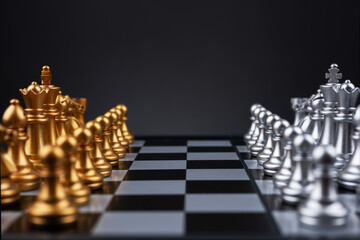 Gold and silver chess figures placed on wooden chessboard. Intellectual duel and tactical battle in...