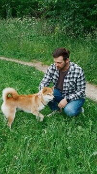 young man in plaid shirt playing training petting hugging and kissing his dog during summer park walk happy loving companionship concept lifestyle	