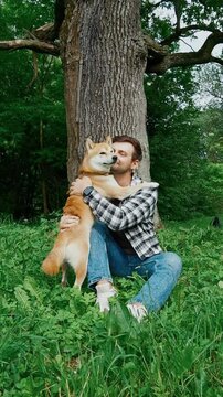 young man in plaid shirt playing training petting hugging and kissing his dog during summer park walk happy loving companionship concept lifestyle	