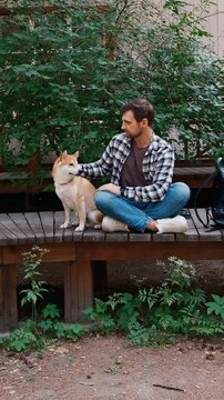 young man in plaid shirt playing training petting hugging and kissing his dog during summer park walk happy loving companionship concept lifestyle	