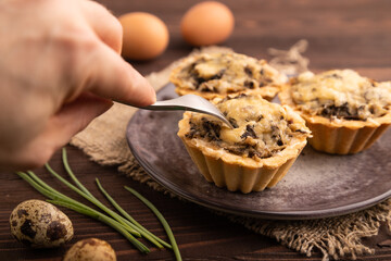Tartlets with meat and cheese with hand on brown wooden, linen textile. side view, close up, selective focus