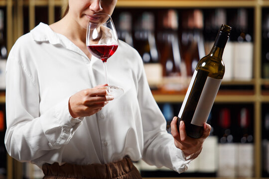 Young beautiful woman sommelier tasting red wine in the wine cellar, close up photo. Alcoholic beverages degustation. Winemaking school, wine waiter certification.