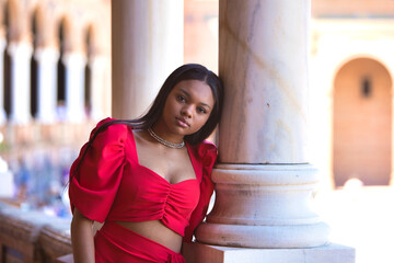 African woman, with long brown hair, young and beautiful, dressed in an elegant red dress, rests...