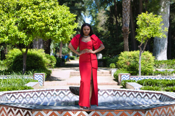 African woman, with long brown hair, young and beautiful dressed in an elegant red dress standing...