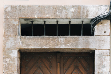 Upper part of the doorway of an old house with iron bars and electric wires in casings. Stone...