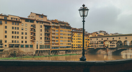 ponte vecchio side with light post florence italy with water reflections and cloudy sky