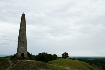 A tall stone obelisk stands on a grassy hilltop in Zagajicka Brda, Serbia, overlooking the landscape and surrounded by open space