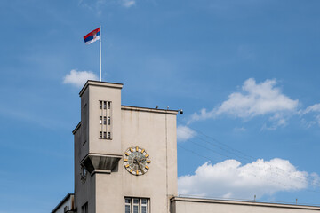 Turm mit Uhr und serbischer Flagge vor blauem Himmel