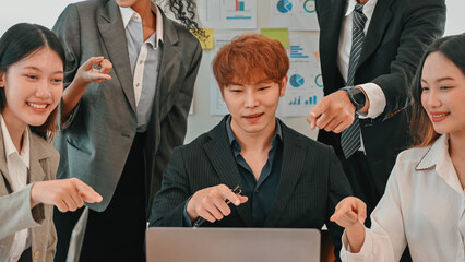 Diverse business team pointing and collaborating around a laptop during a strategy meeting