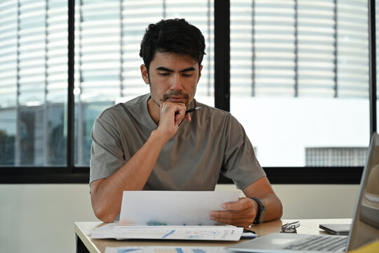 A Businessman analyzing data while seated at a office desk with charts and a laptop