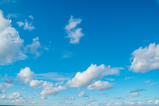 A vast expanse of bright blue sky dotted with fluffy white clouds.Several clouds of varying sizes are scattered across the blue background.This evokes a sense of open space and a peaceful atmosphere