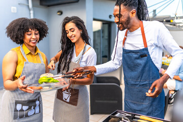 Happy friends grilling meat and vegetables at barbecue party on rooftop