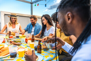 Happy friends eating burgers and hot dogs at rooftop party