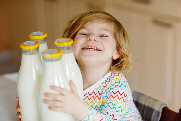 Adorable toddler girl drinking cow milk for breakfast. Cute baby daughter with lots of bottles....