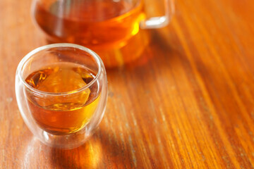Tea time. Pouring black tea into glass cup on wooden table. Close up, top view of hot tea in transparent glass.	