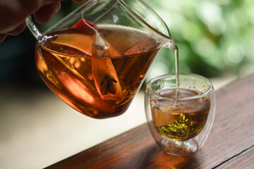 Tea time. Pouring black tea into glass cup on wooden table. Close up, top view of hot tea in transparent glass.	