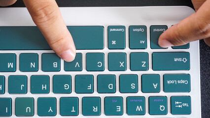 Finger pressing control and V or ctrl + V shortcut keys for paste on a green wireless computer keyboard isolated on black background