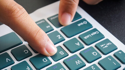 Finger pressing S letter button of a green modern wireless computer keyboard isolated on black...