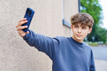 Portrait of smiling teenage schoolboy taking a selfie with smartphone. Happy teen boy on video call, looking confidently at the camera. Real life, real people, modern youth lifestyle concept