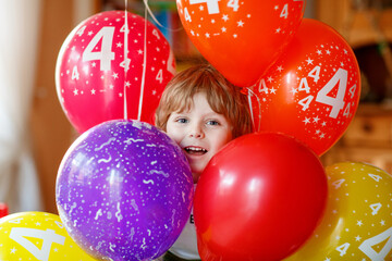 Happy little preschool boy celebrating his 4 birthday with colorful balloons, indoor in kidsroom. Cute excited child having fun.