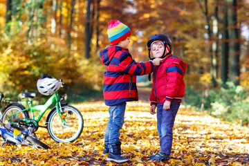 Two little kid boys with bicycles in autumn forest putting helmets